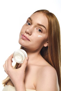 Işıl ışıl ciltli genç bir kadın özenle krem sürüyor, yeni ve doğal bir görünüm sergiliyor..