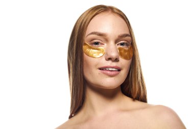 Genç bir kadın altın göz maskeleriyle cilt bakımı seansından zevk alıyor, kendine güven ve güzellik saçıyor..
