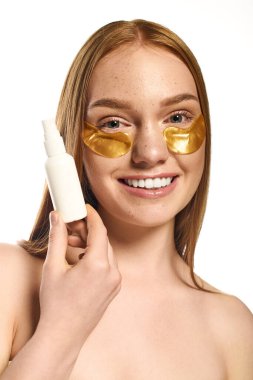 Neşeli genç kadın gençleştirme için altın göz bandı takarken cilt bakım ürünleri uyguluyor..