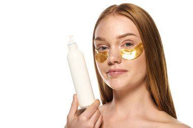 Gülümseyen genç kadın bir deri şişesi tutuyor ve altın göz bantlarını gösteriyor, kendine güveni yayıyor..