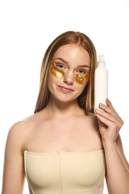 Altın göz bantlı genç bir kadın kendine güvenen bir cilt bakımı ürünü taşıyor..