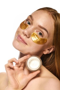 Genç bir kadın, altın göz bantları ve elinde kremle kendi başının çaresine bakmayı sever..