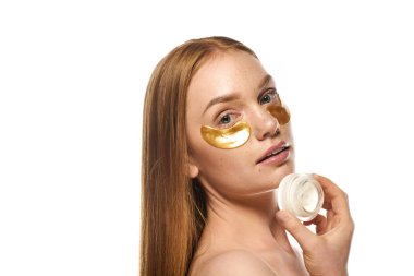 Güzel, genç bir kadın rahatlatıcı bir krem sürerken altın göz maskesi kullanır..