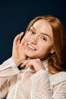 Kızıl saçlı genç bir kadın neşeli bir ifade sergiliyor, benzersiz makyaj detaylarını vurguluyor..