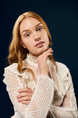 Dalgalı saçlı genç bir kadın beyaz bir elbise içinde zarif bir şekilde poz veriyor..