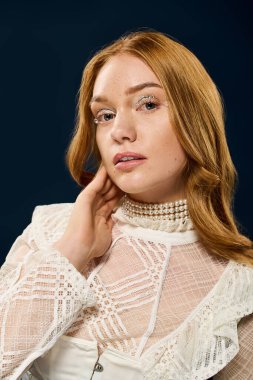 Genç bir kadın zarif poz veriyor, çilli tenini ve şık dantel kıyafetini vurguluyor..