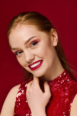 Kırmızı rujlu, gülümseyen genç bir kadın çenesine dokunuyor..