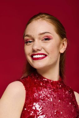 Işıl ışıl gülümseyen genç bir kadın canlı kırmızı bir arkaplanda kendine güvenir..