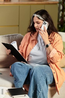 Modern bir dairede, Waardenburg sendromu olan bir kadın notları incelerken telefonla konuşur..