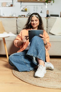 Beyaz perçemli bir kadın evde rahatlıyor, tabletini yerde kullanıyor..