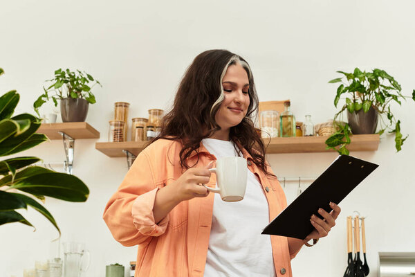 A woman with a white forelock smiles as she holds a cup of coffee and examines a clipboard.