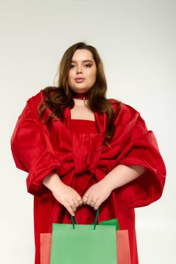 Büyük kurdeleli, parlak kırmızı elbiseli neşeli, iri yarı bir kadın bayramı kutluyor..