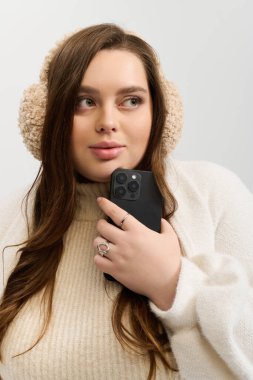 Genç bir kadın, parlak bir stüdyo ortamında elinde telefonuyla örülü bir kazakla neşe saçıyor..