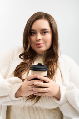 Genç ve iri bir kadın elinde kahve fincanı tutarken örgü örüp poz veriyor..