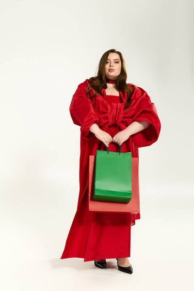 A plus-size woman in a red outfit holds holiday bags, celebrating the festive cheer.