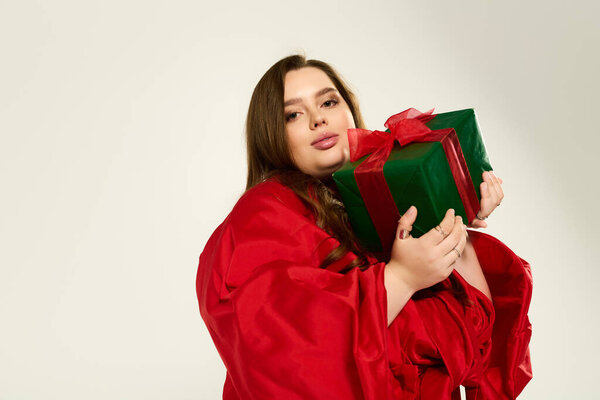 Молодая женщина в ярко-красном костюме с радостью держит завернутый подарок во время празднования.