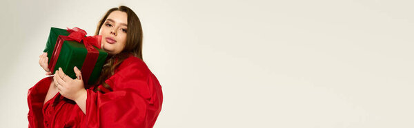 A young plus size woman in a vibrant red outfit happily embraces holiday gifts, banner