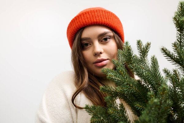 Young woman in a knitted winter sweater poses with a playful attitude amidst greenery.