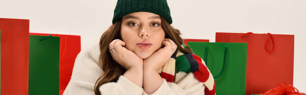 Радостная молодая женщина в зимнем наряде расслабляется среди красочных рождественских подарков, баннера