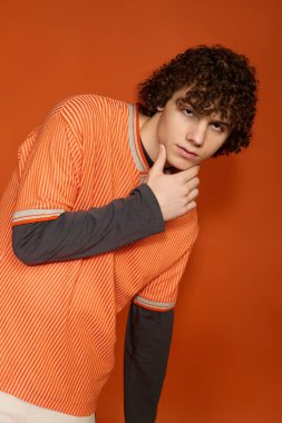 Genç bir kız kendine güvenerek poz veriyor, parlak turuncu bir ortamda modaya uygun giyiniyor..