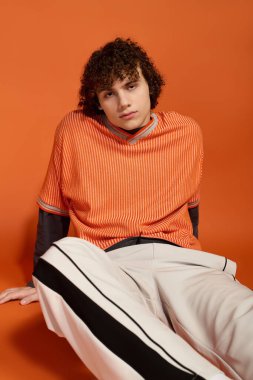 Günlük giysiler içindeki bir çocuk, parlak turuncu bir arka planda eşsiz tarzını ön plana çıkarıyor..