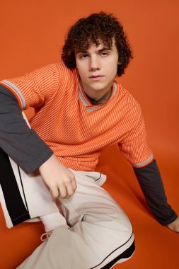 Kıvırcık saçlı genç bir çocuk. Parlak bir arkaplanda günlük giysiler giyiyor..