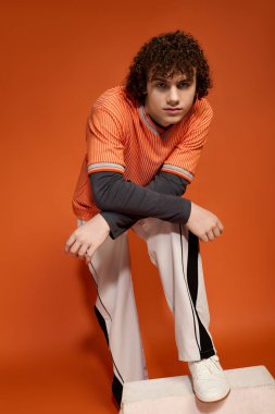 Kıvırcık saçlı genç bir çocuk, güncel eğilimleri vurgulayarak günlük giysiler içinde poz veriyor..