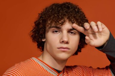 Kıvırcık saçlı genç, parlak turuncu bir arka planda duruyor..