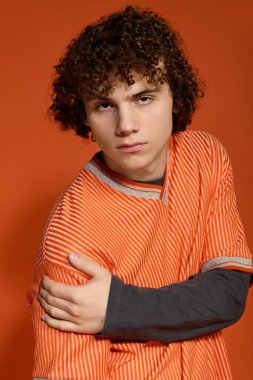 Kıvırcık saçlı bir genç düşünceli bir poz verirken sıradan giyinir..