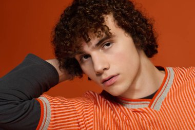 Kıvırcık saçlı genç cesur turuncu arka planda sıradan moda sergiliyor..