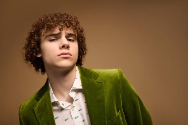 Şık bir stüdyoda, kıvırcık saçlı bir genç canlı yeşil bir ceket giyer ve kendine güveni yayar..