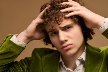 Kıvırcık saçlı genç bir çocuk, tarzını yeşil ceketli, düşünceli poz verirken sergiliyor..