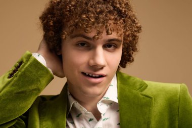 Kıvırcık saçlı, kendine güvenen bir genç çocuk yeşil kadife ceketle poz veriyor..