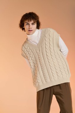 Kıvırcık saçlı genç bir çocuk atölyede örülmüş bir yelek içinde poz veriyor..