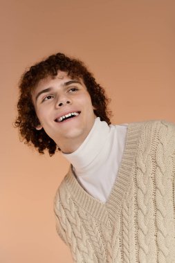 Kıvırcık saçlı neşeli genç bir çocuk örgü bir yelek içinde poz veriyor.