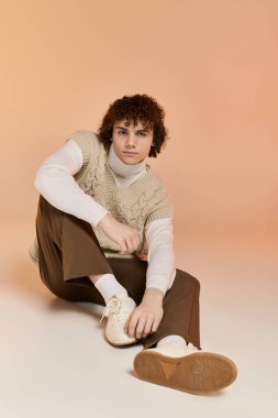 Kıvırcık saçlı genç bir çocuk örülmüş bir yelek içinde şık bir şekilde oturur ve kış havasını kucaklar..