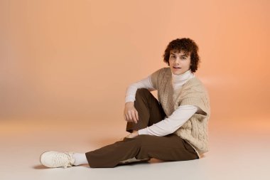 Kış sıcağını kucaklayan kıvırcık saçlı genç bir çocuk örgü bir yelek içinde şık poz verir..