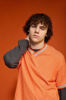 Kıvırcık saçlı genç bir çocuk rahat bir şekilde ayakta duruyor, canlı bir görünüm yaratıyor..