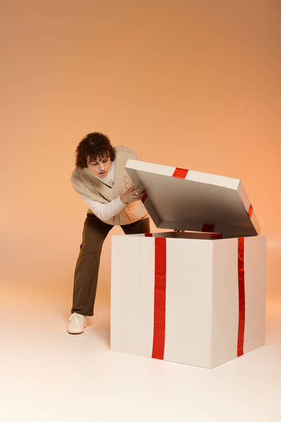 Кудрявый мальчик открывает большую подарочную коробку в уютной студии во время праздников.