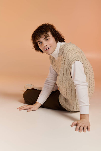 A curly-haired teenager wears a knitted vest, sitting in a warm studio