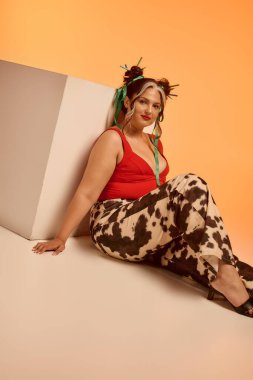 Beyaz perçemli genç bir kadın turuncu arka planda rahatça poz veriyor..