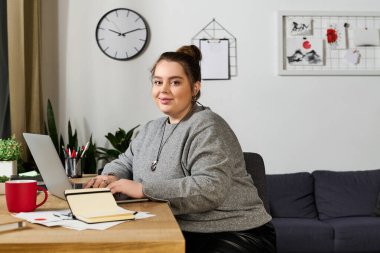 Rahat bir çalışma alanında, büyük beden bir kadın bilgisayarında yaratıcı bir şekilde çalışıyor..