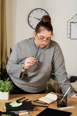 Güzel ve iri yarı bir kadın düşünceli bir şekilde rahat bir masadaki yaratıcı işine odaklanır..