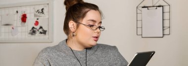 Ayrıca boydaki kadın, sanatla dolu sıcak ve davetkar bir yerde, tabletin üzerinde dikkatle okuyor..