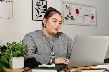 Kadınlar şık bir çalışma alanında dizüstü bilgisayarıyla uğraşırken rahat bir süveter giyerler..