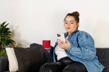 Kanepede dinlenirken, güzel ve iri yarı bir kadın sıcak bir içkiyi yudumlarken telefonuna bakar..