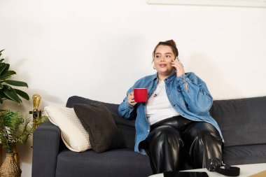 Güzel ve iri yarı bir kadın, telefonda kırmızı bardaktan yudumlayarak koltukta dinlenir..