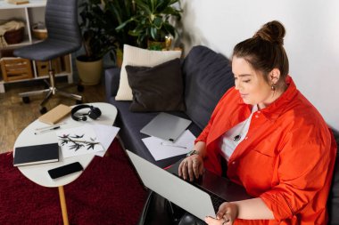 Güzel, iri yarı bir kadın kanepeye oturur ve laptopuna odaklanır..