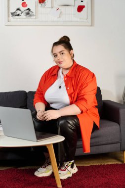 Kendine güvenen, iri yarı bir kadın şık bir koltukta oturur dizüstü bilgisayarını incelerken, sıcaklık yayar..