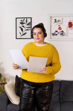 Ayrıca evde müzik dinlerken parlak kazak giyen cüsseli bir kadın gazeteleri tutuyor..